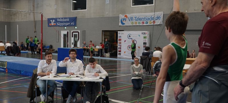 Blick in die Turnhalle mit einem jungen Turner, der auf die Freigabe für seine Übung an den Ringen wartet